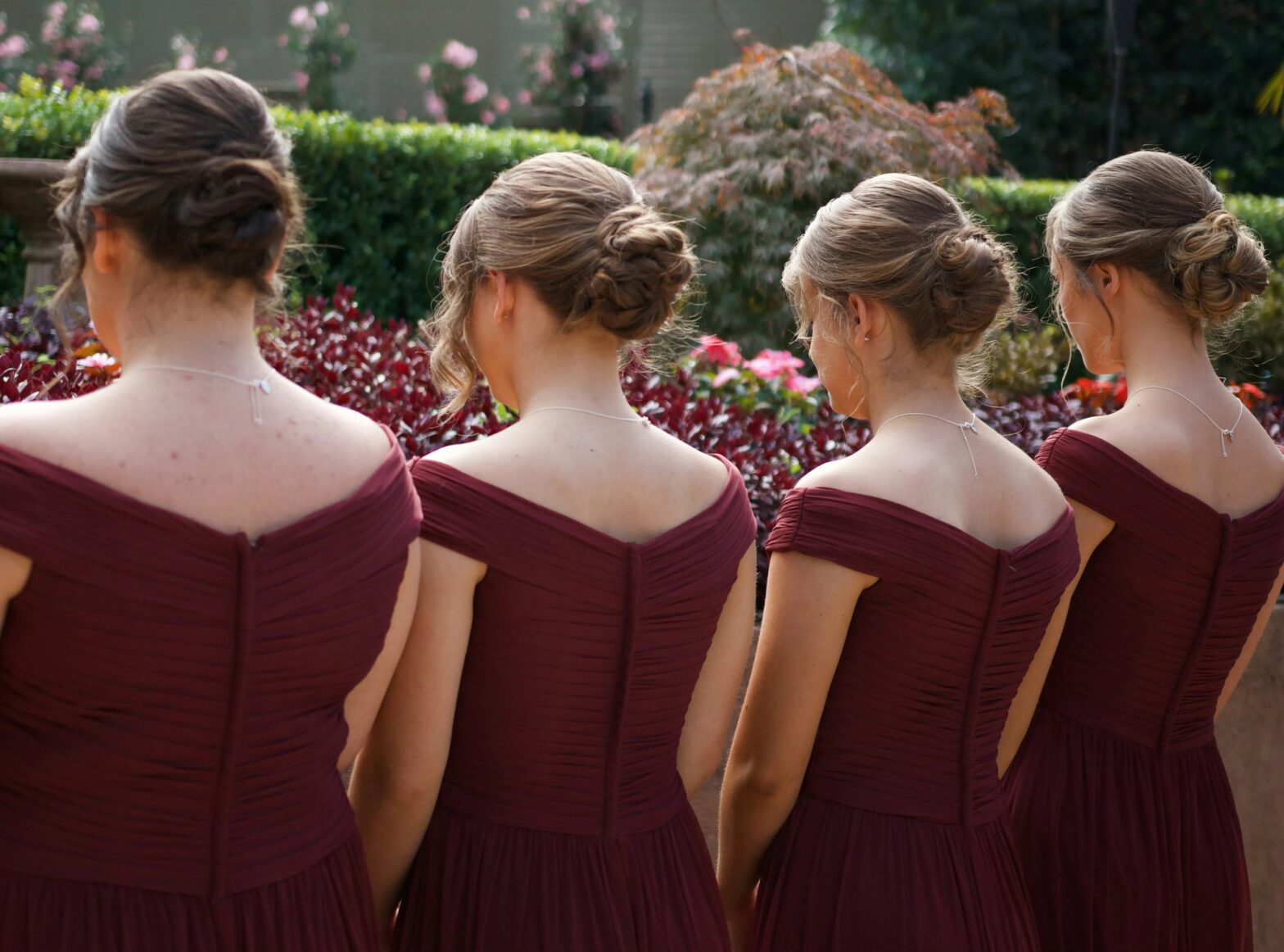4 bridesmaids facing away from the camera, wearing burgundy bridesmaid dresses.